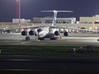 A large cargo aircraft parked on an airport runway at night, under bright lights.