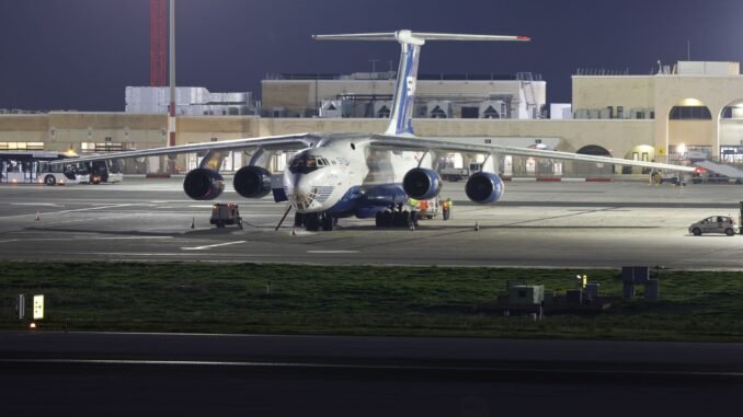 A large cargo aircraft parked on an airport runway at night, under bright lights.
