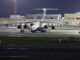 A large cargo aircraft parked on an airport runway at night, under bright lights.