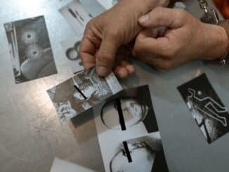 Close-up of handcuffed person examining crime scene photos on table, indicating investigation process.
