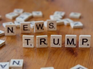 Wooden letter tiles spell 'NEWS' and 'TRUMP' on a wooden table, relating to political discourse.
