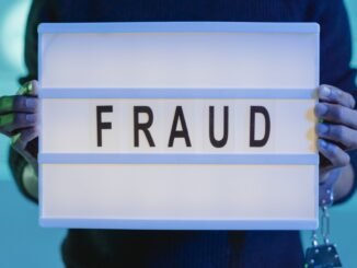 Close-up of hands holding a sign with 'fraud', illuminated in blue light.