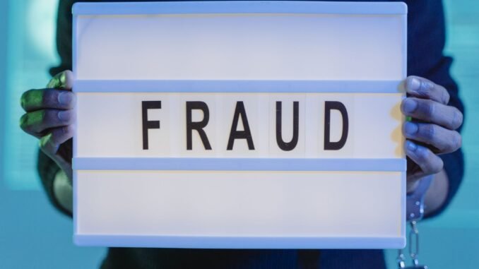 Close-up of hands holding a sign with 'fraud', illuminated in blue light.