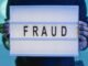 Close-up of hands holding a sign with 'fraud', illuminated in blue light.