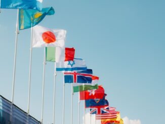 A row of international flags waving under a clear blue sky in Paris, France.