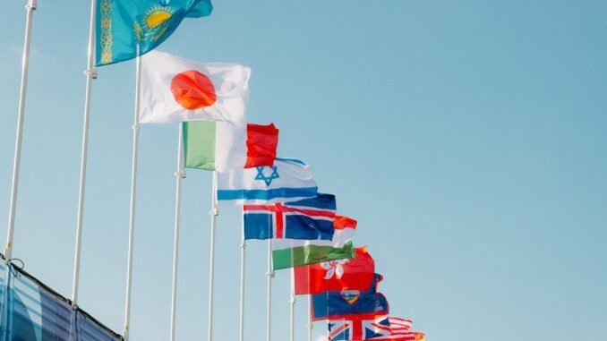 A row of international flags waving under a clear blue sky in Paris, France.