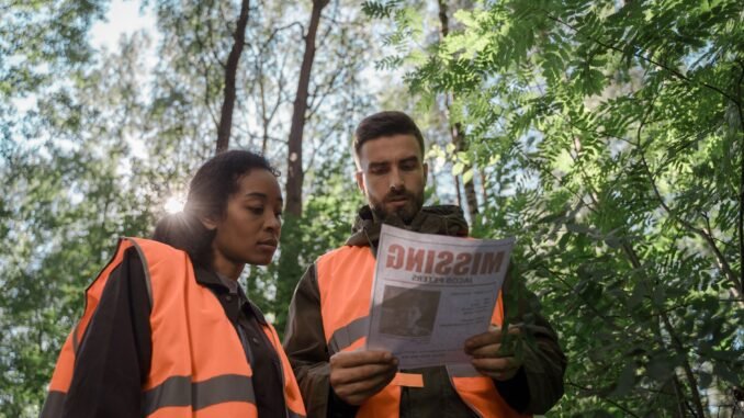 Team members in safety vests examine a missing person flyer in a forest setting.