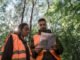 Team members in safety vests examine a missing person flyer in a forest setting.